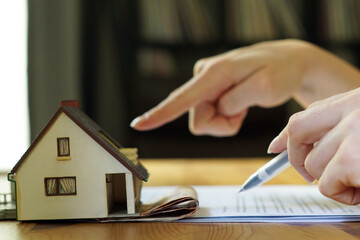 A closeup of a hand holding a pen next to the miniature house 