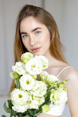 Obraz na płótnie Canvas Cute happy young girl in white blank t-shirt, holding a bouquet and looks at the of flowers, enjoying the smell. beautiful blond teen girl with braces on her teeth smiling