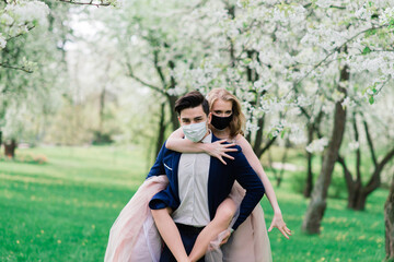 Young loving couple walking in medical masks in the park during quarantine on their wedding day. Coronavirus, disease, protection, sick, illness flu europe celebration canceled.