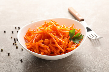 Fork and bowl with carrot salad on gray background, close up