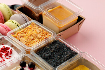 Mousse desserts in square plastic boxes with different toppings on pink table