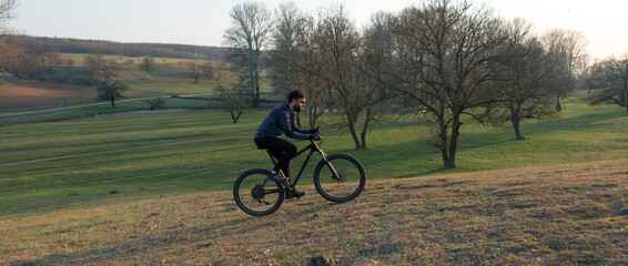 Fototapeta premium Cyclist in shorts and jersey on a modern carbon hardtail bike with an air suspension fork standing on a cliff against the background of fresh green spring forest