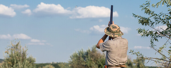 Silhouette of a hunter with a gun in the reeds against the sun, an ambush for ducks with dogs