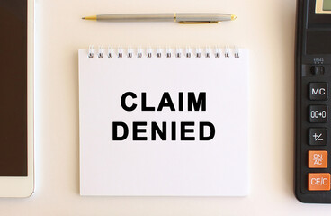 Notepad with text CLAIM DENIED on a white background, near calculator, tablet and pen. Business concept.