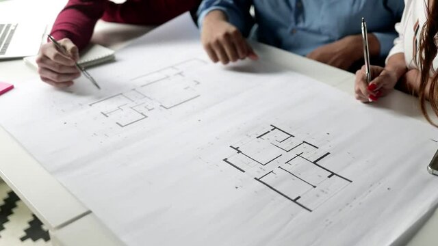 Group of business people discussing blueprint, meeting and talking at table and working on building floor plan. Cropped shot, high angle. Architecture or paperwork concept
