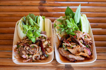 Close up Popular Thai cuisine, spicy sliced grilled pork salad recipe for Larb Nam Tok with mint leaves on top on wooden table background . Traditional food of Thailand . Thai north eastern food .