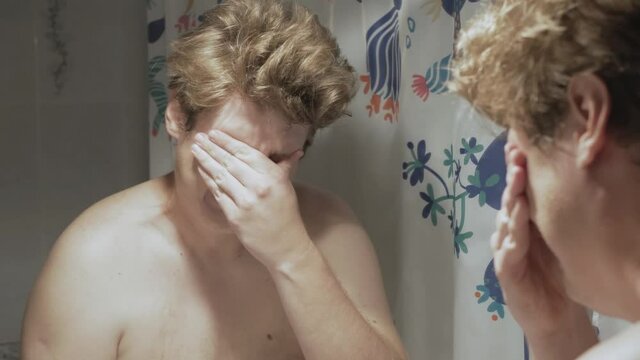 Young fat Caucasian man looks at the mirror and cries