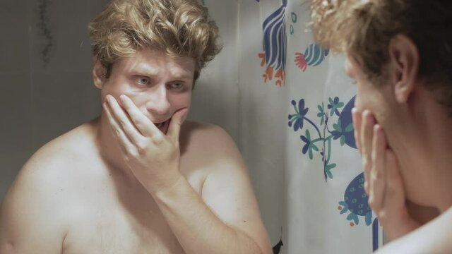 Young fat Caucasian man looks at the mirror and cries