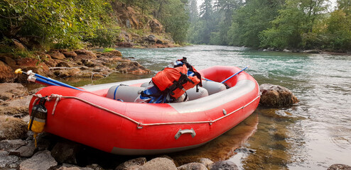 Red raft on edge of beautiful river with backpack and ores resting inside - obrazy, fototapety, plakaty