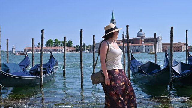 A woman in a hat in Venice stands at the canal. Traveling around Europe in Italy. Persona poses in the frame, positive emotions.