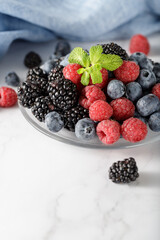 Assorted berries with mint sprigs on a glass plate
