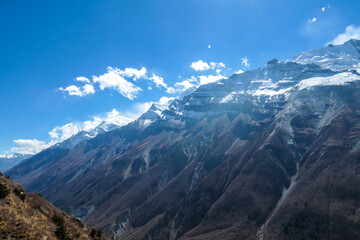 Obraz na płótnie Canvas A panoramic view on sharp and dangerous, high, snow capped Himalayan peaks long Annapurna Circuit in Nepal. Slopes are overgrown with small bushes. Exploration and discovering. Steep mountain wall.