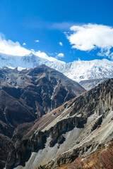 Fototapeta na wymiar A panoramic view on a valley along Annapurna Circuit in Nepal. In the back there are high, snow capped Himalayan peaks. Slopes are overgrown with small bushes. Exploration and discovering