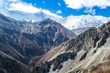 A panoramic view on a valley along Annapurna Circuit in Nepal. In the back there are high, snow capped Himalayan peaks. Slopes are overgrown with small bushes. Exploration and discovering
