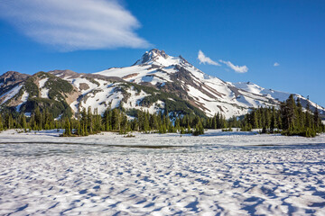 Volcanic mountain peak under a crisp blue sky rises behind a field of snow. 
