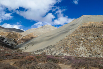 Harsh and golden colored slopes in Manang Valley, Annapurna Circus Trek, Himalayas, Nepal, with the view on Annapurna Chain and Gangapurna. Dry and desolated landscape. High snow capped mountain peaks