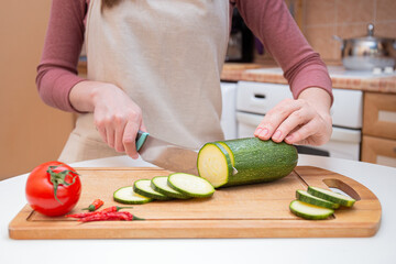 Close-up Hands of a young woman cut with a knife into slices or slices of young zucchini cucumber on a wooden cutting board. Preparation of ingredients and vegetables before cooking and for grilling
