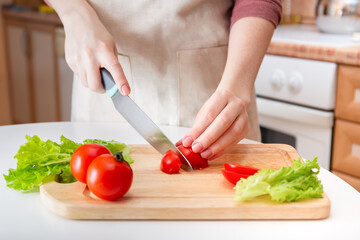 Female hands cut a juicy red tomato into slices with a knife on a wooden cutting board. A method of preparing vegetables and ingredients before cooking