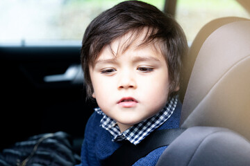 Portrait cut lilttle boy sitting in a car in safety chair, Adorable toddler boy sitting in car seat, Child in car seat looking down and thniking face with belt on shoulder, Child transportation safety