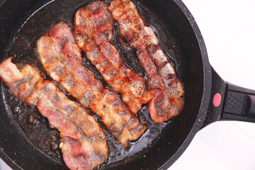 Bacon strips or rashers being cooked in frying pan. Hearty high-calorie breakfast. Fast food, unhealthy food