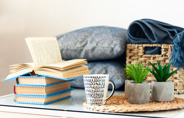 Obraz na płótnie Canvas Cozy home interior decor: stack of books, plants in pots on a wicker stand, pillows and plaid on a white table. Distance home education. Quarantine concept of stay home.