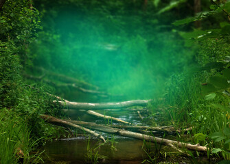 Light blue mist in green forest over little river with lying logs. Transparent turquoise haze on blurry background. Summer landscape