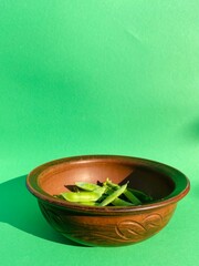 Young green peas lies in a brown clay plate stands on a green background