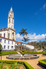 Fototapeta na wymiar Old neo-Gothic church and side buildings of the sanctuary complex, seen from the garden, with blue sky in the background, Caraca Sanctuary, city of Catas alta, state of Minas Gerais, Brazil