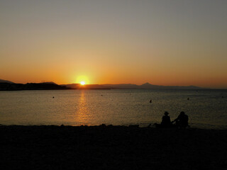 A couple looking at the sunset on a rockbeach. Two people looking the sundown on a beach