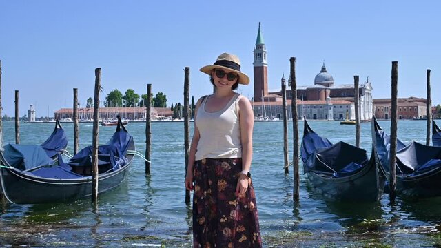 A woman in a hat in Venice stands at the canal. Traveling around Europe in Italy. Persona poses in the frame, positive emotions.