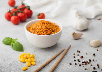 White bowl plate with boiled red long grain basmati rice with vegetables on light table background with sticks and tomatoes with corn,garlic and basil.