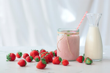 Strawberry milk shake in a glass jar. Milk in a glass jug, some strawberries around. White background