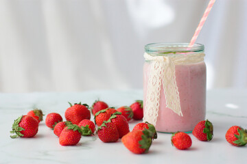 Strawberry milk shake in a glass jar with a pink stick and lace ribbon. Some strawberries around. White background