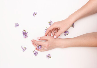 Obraz na płótnie Canvas Concept of hand care, anti-wrinkle, anti-aging cream, Spa. Beautiful female hands with lilac flowers on a white background, top view.
