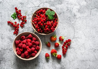 Fresh ripe berries in bowls - raspberries, red currant strawberries on a gray background, top view