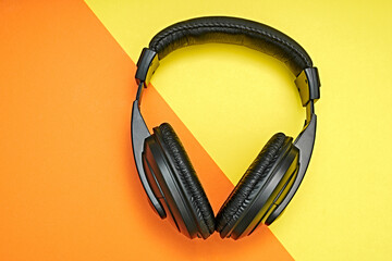 Large, black headphones lie on a colored background. Device for individual listening to music.