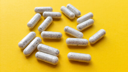 White pill capsules on yellow background. Simple flat lay with pastel texture. Medical concept. Stock photo.