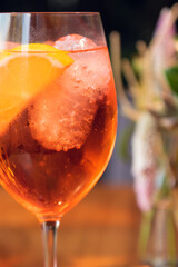 Orange cocktail with orange garnish in wine glass, aperol spritz in sunny setting.