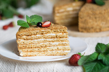 Piece of cake with honey shortcakes with sour cream, berries and mint on a white plate.