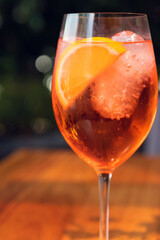 Orange cocktail with orange garnish in wine glass, aperol spritz in sunny setting.