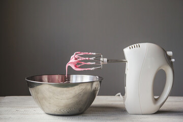 Pink butter cream in a metal bowl. Beating cream cake. Mixer whisk in cream...