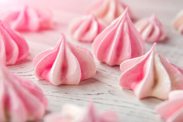 Little pink meringues on a white wooden table.