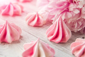 Little pink meringues on a white wooden table. Pink peony flower.