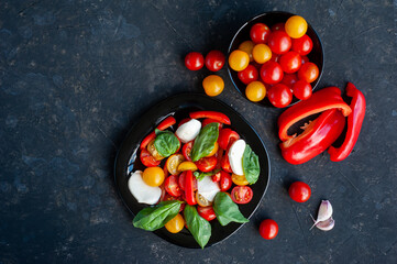 Red and yellow cherry tomato salad with pepper, basil and mozzarella on a dark background.