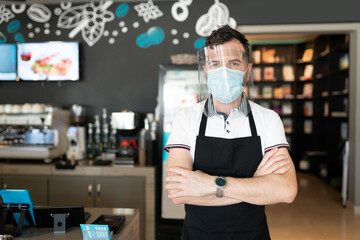 Fototapeta na wymiar Man With Face Shield And Mask Working In Cafe