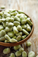 Fresh broad beans in a ceramic bowl on a wooden table close up view