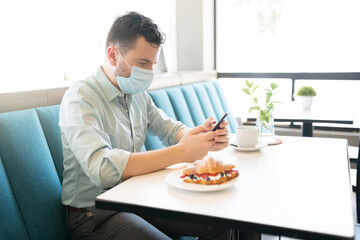 Man In Mask Using Mobile Phone At Cafe