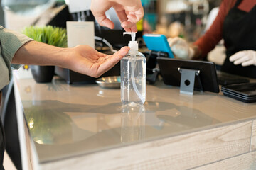 Man Applying Disinfectant On Hand In Cafe