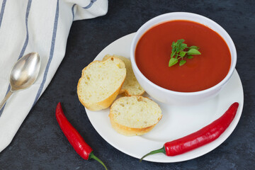 Summer diet cold gazpacho soup of tomato in a white bowl, pepper and herbs on a black background. Sliced bread for snacks. Vegetarian food