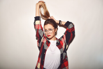 A sad girl holds the ends of the hair in her hands. Hipster model with glasses and a plaid shirt is sad. Girl holds tail in hands and shows a sad face